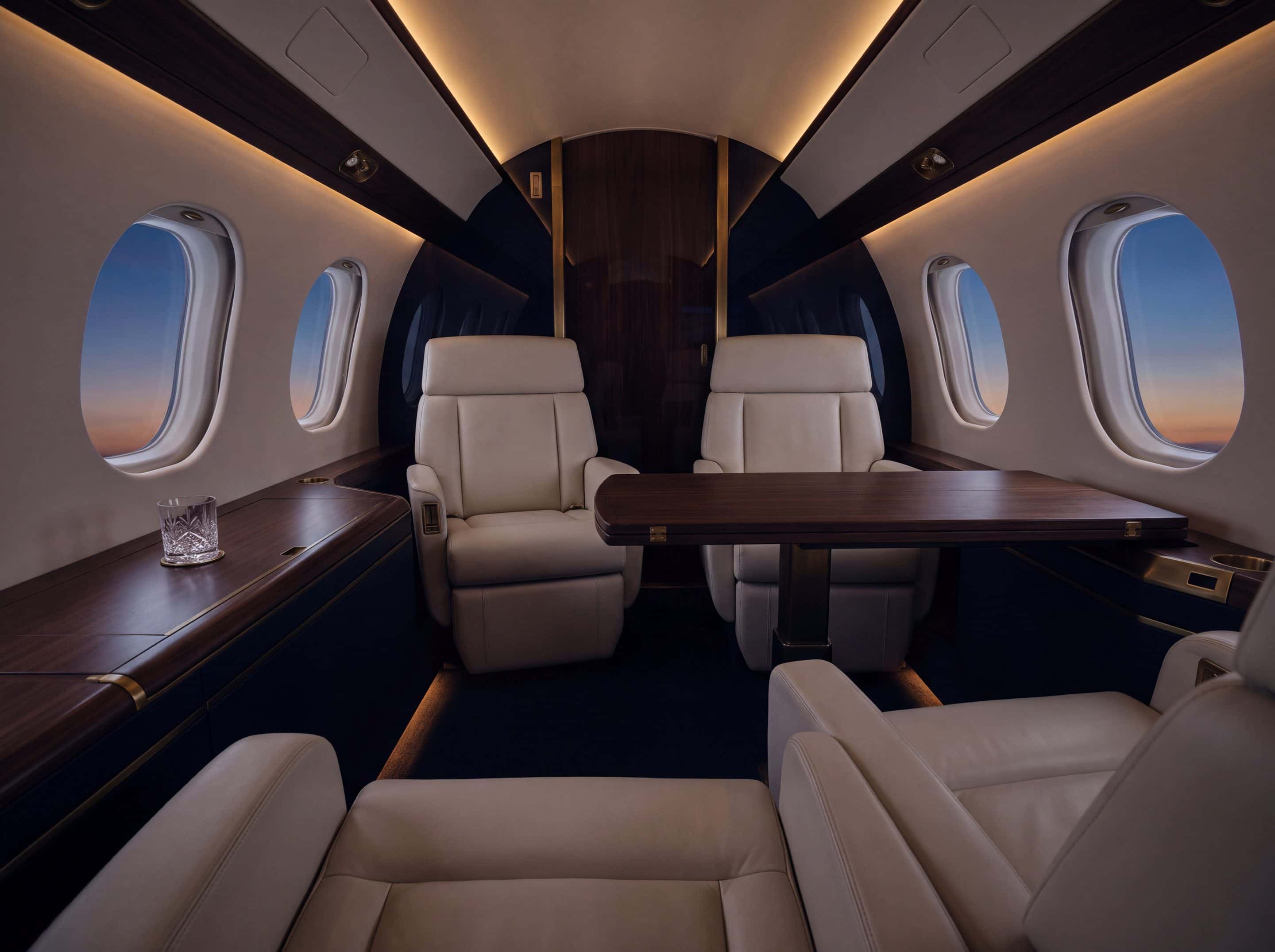 Cabina de un jet de cabina amplia en penumbra cálida, con butacas de cuero claro y mesa de madera